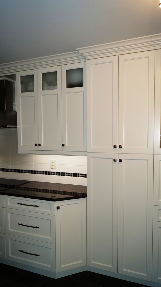 Example of a trendy galley eat-in kitchen design in Montreal with an undermount sink, shaker cabinets, white cabinets, granite countertops, white backsplash, ceramic backsplash and stainless steel appliances
