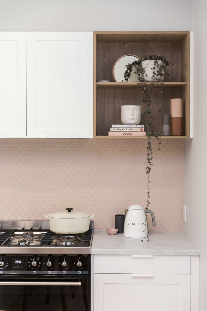 Exempel på ett litet minimalistiskt vit vitt kök, med en undermonterad diskho, luckor med infälld panel, vita skåp, bänkskiva i kvarts, rosa stänkskydd, stänkskydd i mosaik, svarta vitvaror, mellanmörkt trägolv och en köksö