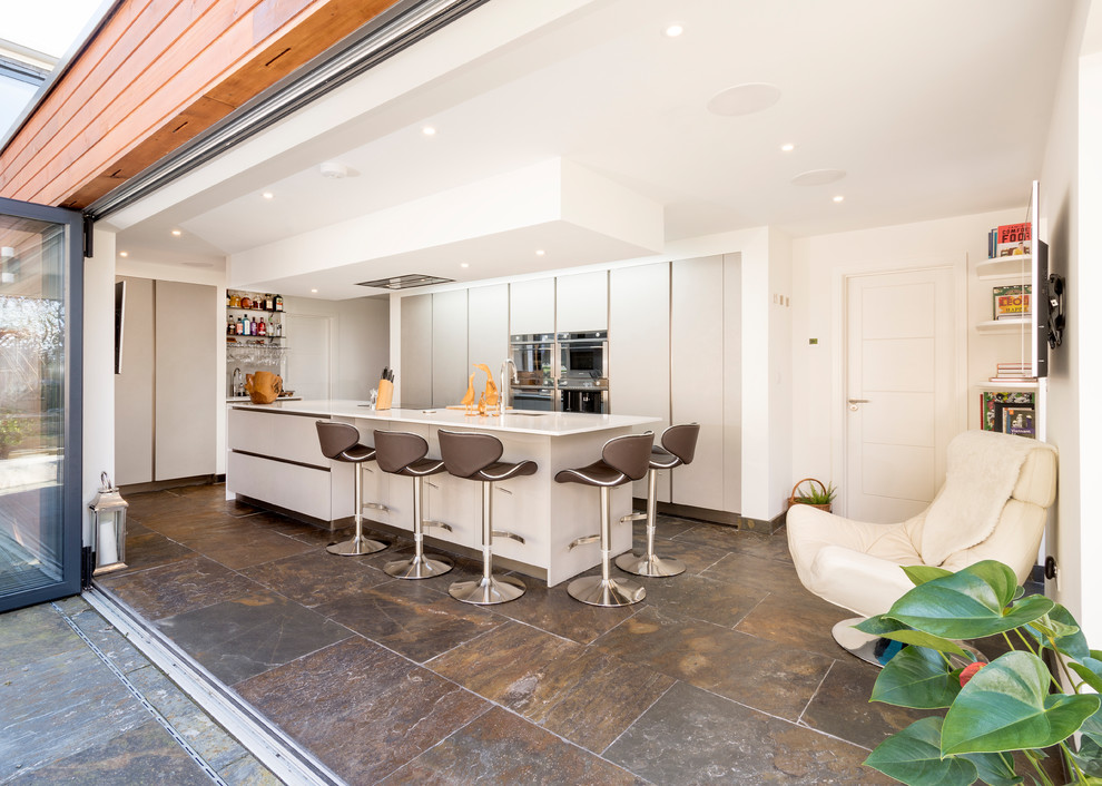 Moderne Küche ohne Insel mit integriertem Waschbecken, flächenbündigen Schrankfronten, Mineralwerkstoff-Arbeitsplatte, Schieferboden und weißer Arbeitsplatte in Devon