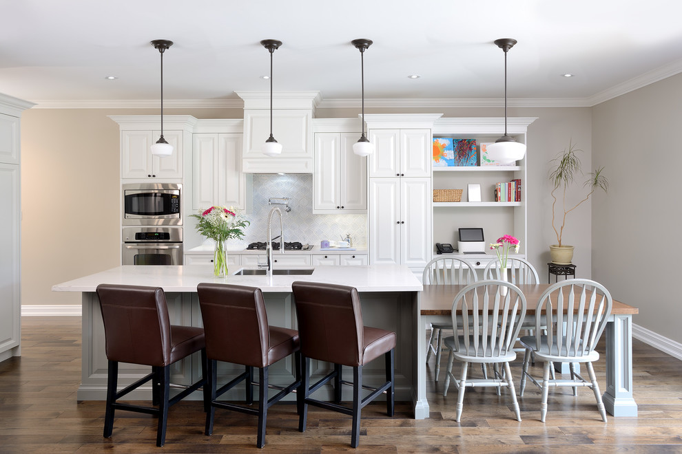 Exempel på ett klassiskt kök, med en undermonterad diskho, vita skåp, bänkskiva i kvarts, grått stänkskydd, rostfria vitvaror, mellanmörkt trägolv och luckor med upphöjd panel