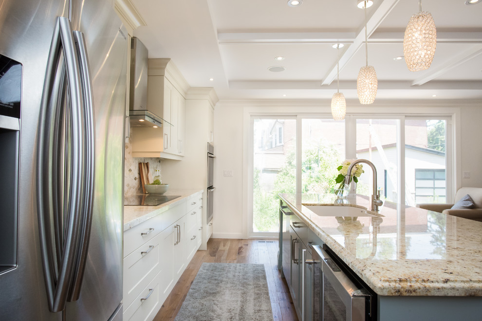 Idée de décoration pour une cuisine américaine linéaire tradition de taille moyenne avec un évier encastré, un placard à porte shaker, des portes de placard blanches, un plan de travail en granite, un électroménager en acier inoxydable, un sol en bois brun et îlot.