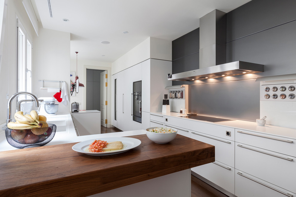 Photo of a large contemporary galley kitchen/diner in Madrid with flat-panel cabinets, white cabinets, black splashback, black appliances, a breakfast bar, engineered stone countertops and dark hardwood flooring.