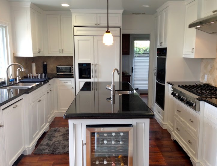 This is an example of a medium sized traditional u-shaped enclosed kitchen in Los Angeles with a double-bowl sink, recessed-panel cabinets, white cabinets, medium hardwood flooring, no island, composite countertops, beige splashback, ceramic splashback, stainless steel appliances and brown floors.