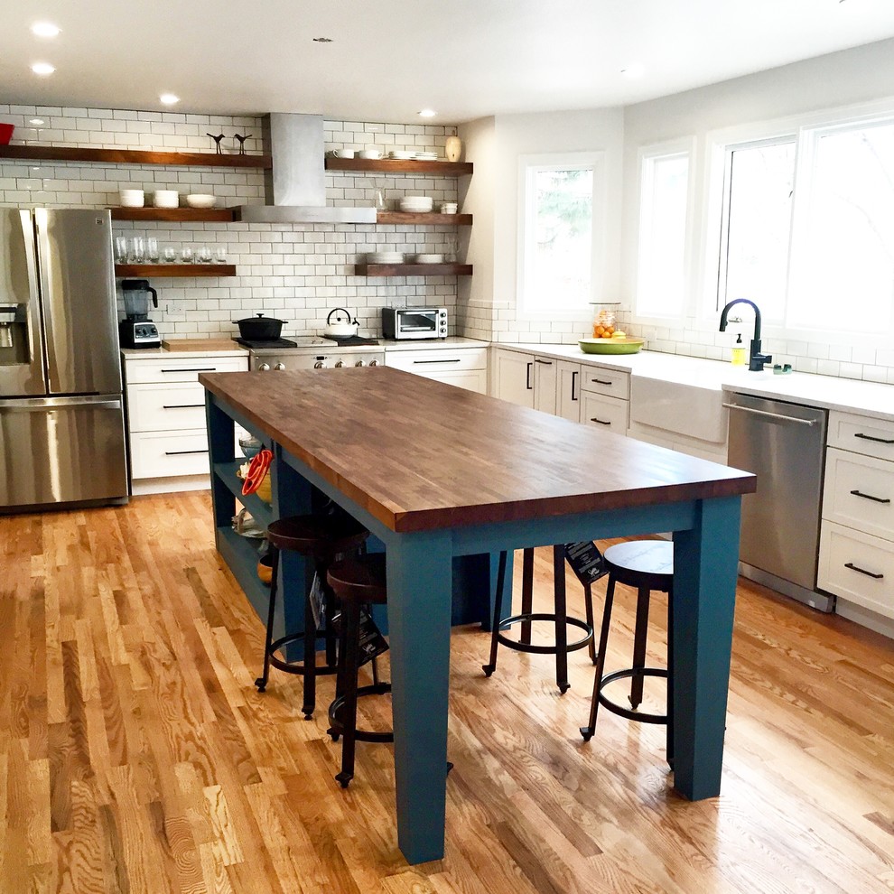 Cottage l-shaped medium tone wood floor eat-in kitchen photo in Phoenix with a farmhouse sink, shaker cabinets, white cabinets, quartzite countertops, white backsplash, subway tile backsplash, stainless steel appliances and an island