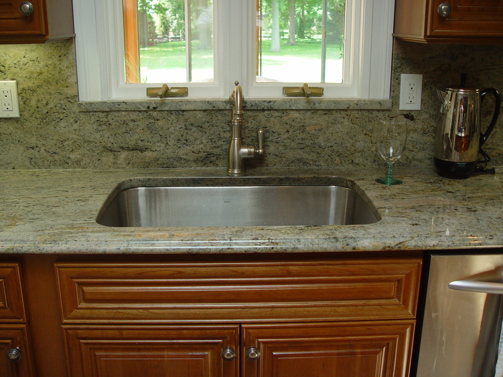 Example of a mid-sized classic l-shaped ceramic tile eat-in kitchen design in New York with an undermount sink, raised-panel cabinets, dark wood cabinets, granite countertops, beige backsplash, stone slab backsplash, stainless steel appliances and an island