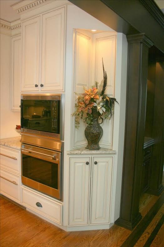 Modelo de cocina tradicional con puertas de armario blancas, encimera de mármol, electrodomésticos de acero inoxidable y suelo de madera clara