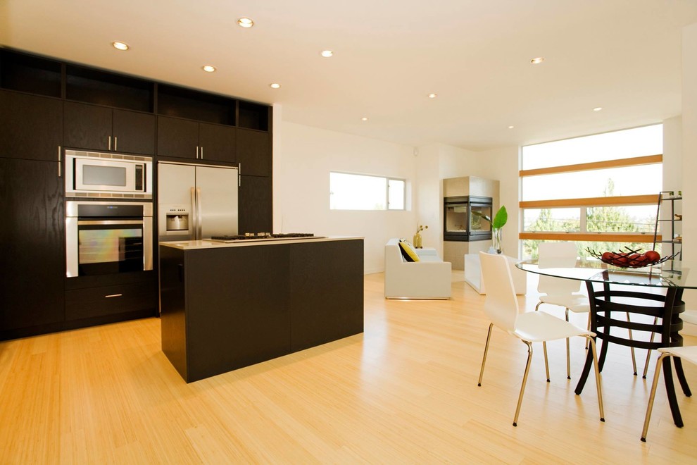 Exempel på ett mellanstort modernt kök, med släta luckor, svarta skåp, bänkskiva i kalksten, rostfria vitvaror, ljust trägolv, en köksö och brunt golv