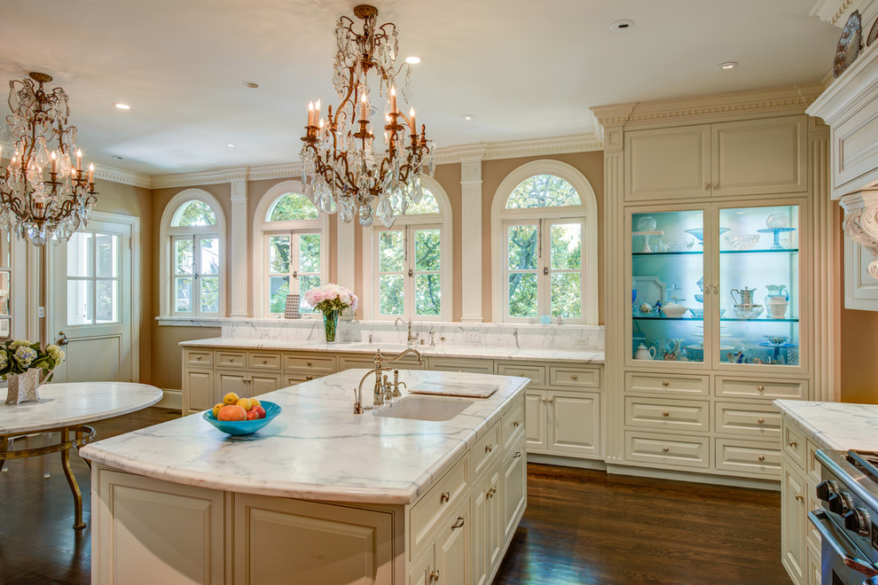 Exempel på ett klassiskt kök och matrum, med en enkel diskho, luckor med glaspanel, vita skåp, vitt stänkskydd, stänkskydd i marmor, mörkt trägolv, en köksö och brunt golv