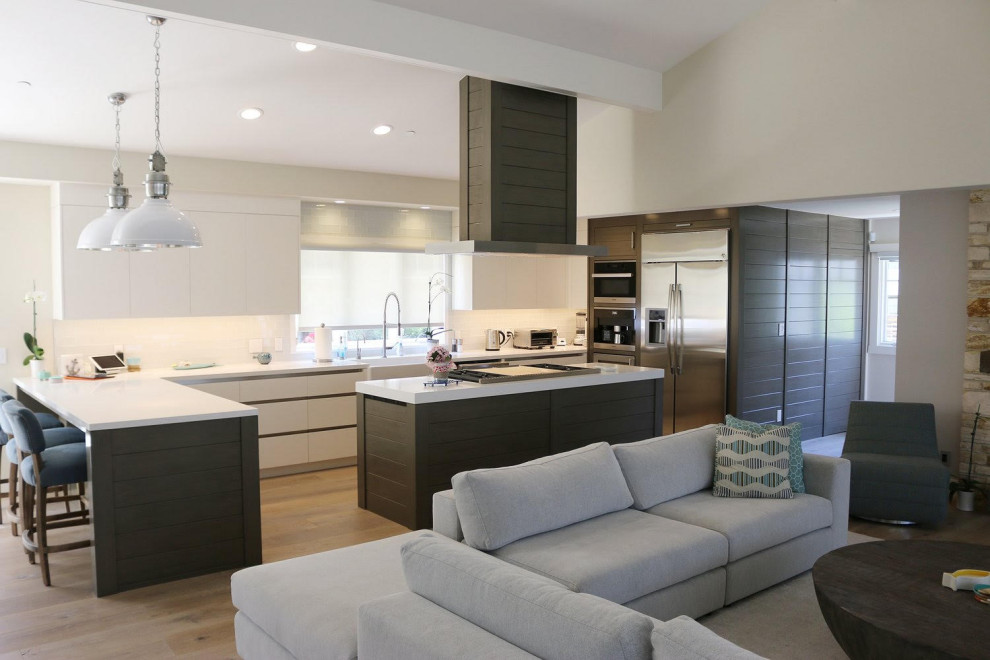 Medium sized l-shaped open plan kitchen with a single-bowl sink, flat-panel cabinets, white cabinets, marble worktops, stainless steel appliances, light hardwood flooring, an island, brown floors and white worktops.