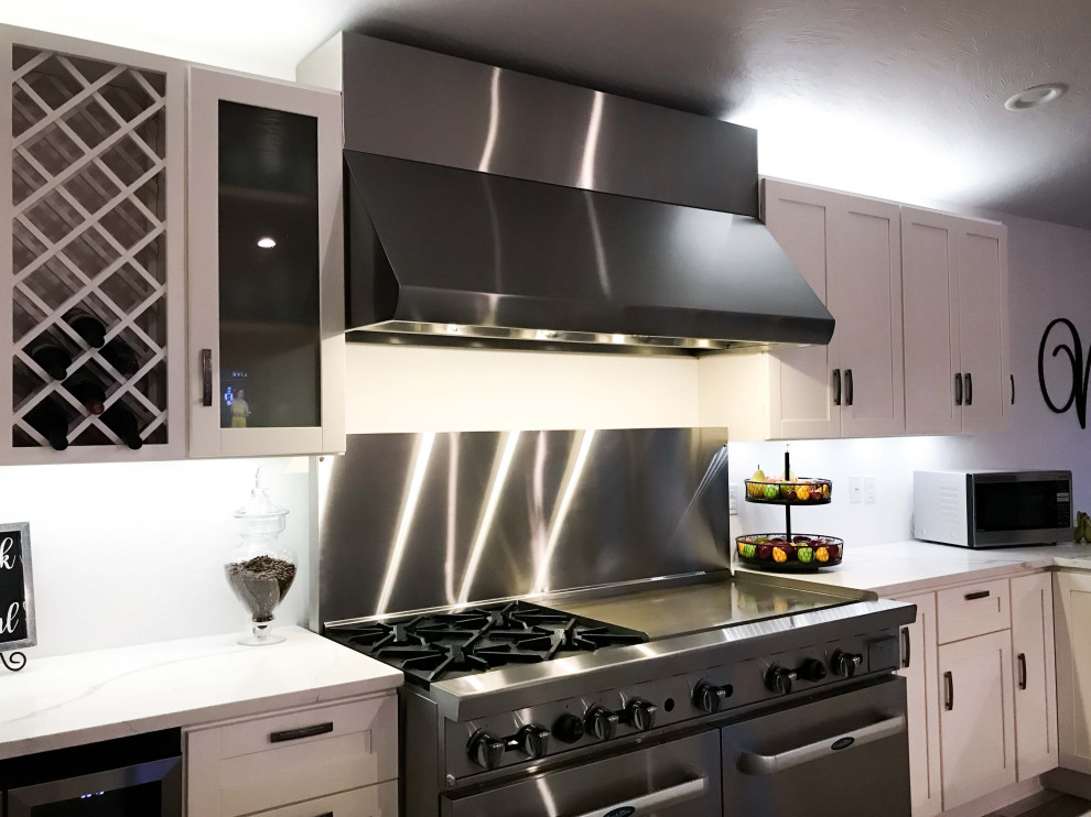 Foto de cocina minimalista de tamaño medio con armarios estilo shaker, puertas de armario blancas, encimera de mármol, salpicadero metalizado, electrodomésticos de acero inoxidable y encimeras blancas