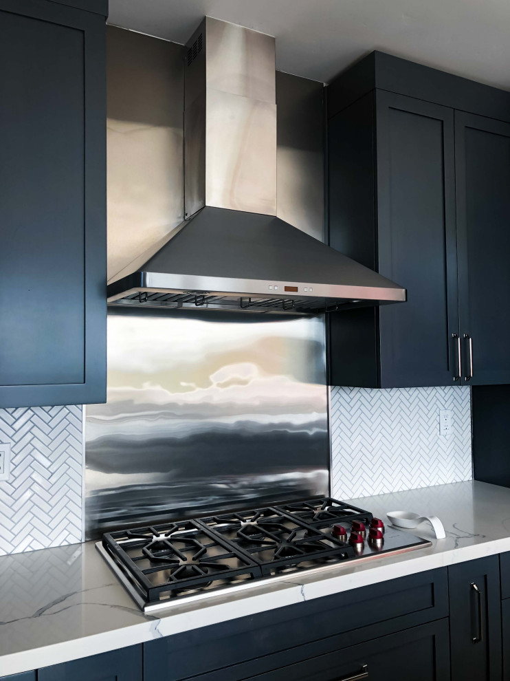 Ejemplo de cocina comedor lineal moderna pequeña con armarios estilo shaker, puertas de armario negras, encimera de mármol, salpicadero metalizado, electrodomésticos de acero inoxidable y encimeras blancas