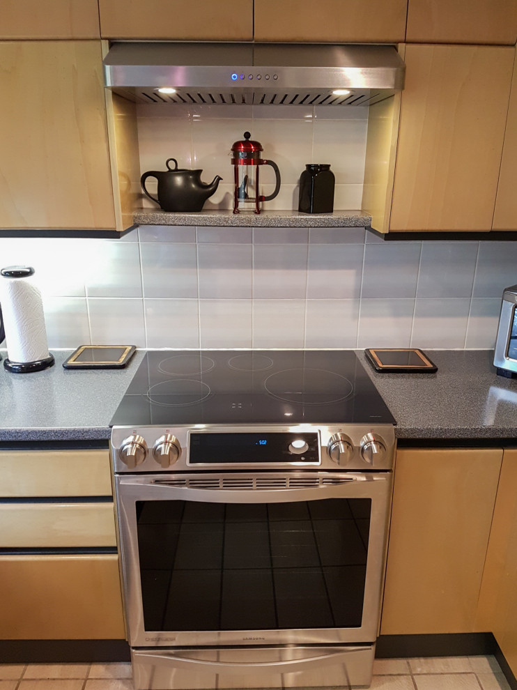 Small modern single-wall kitchen/diner with flat-panel cabinets, light wood cabinets, granite worktops, grey splashback, ceramic splashback, stainless steel appliances and grey worktops.