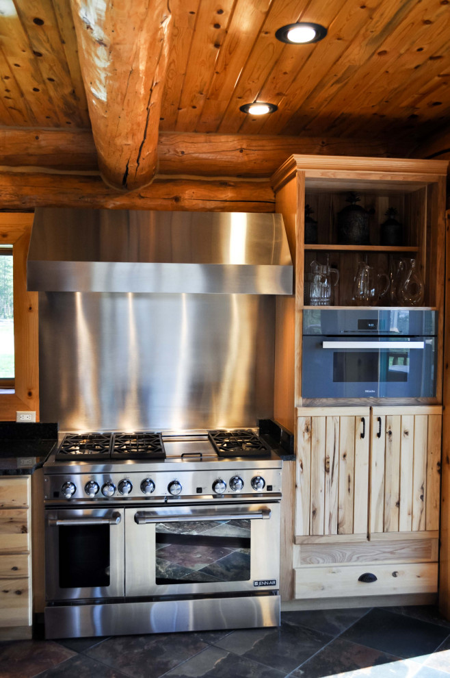 Cette photo montre une cuisine américaine linéaire montagne en bois clair de taille moyenne avec un placard à porte persienne, une crédence métallisée, un électroménager en acier inoxydable, carreaux de ciment au sol et un sol noir.