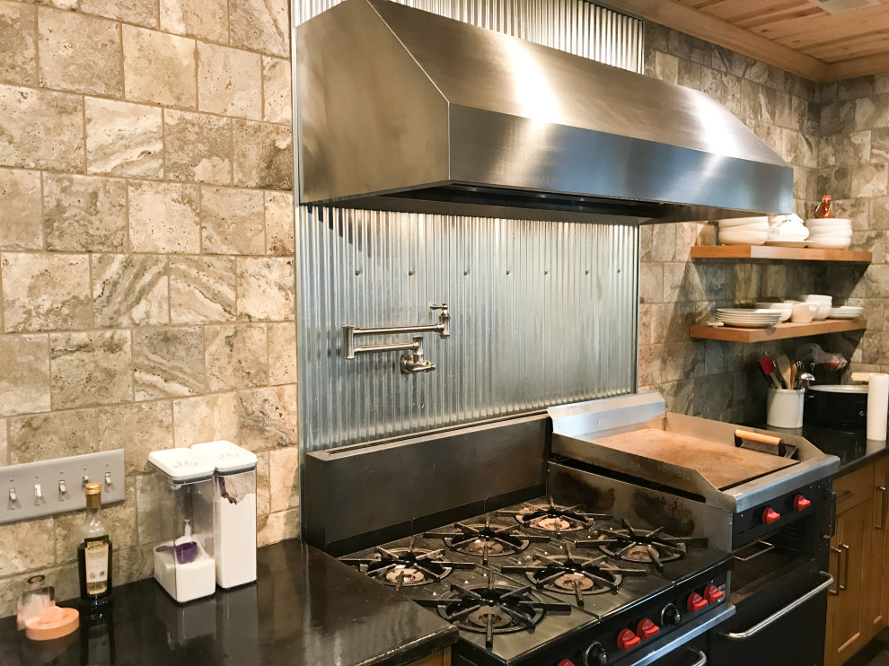 Exemple d'une cuisine américaine linéaire industrielle en bois clair de taille moyenne avec un placard sans porte, un plan de travail en stratifié, une crédence métallisée, un électroménager en acier inoxydable et plan de travail noir.