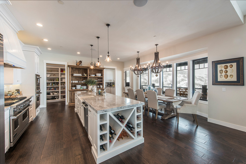 Mid-sized transitional single-wall dark wood floor and brown floor open concept kitchen photo in Salt Lake City with a farmhouse sink, shaker cabinets, white cabinets, white backsplash, stainless steel appliances, an island, gray countertops, marble countertops and marble backsplash