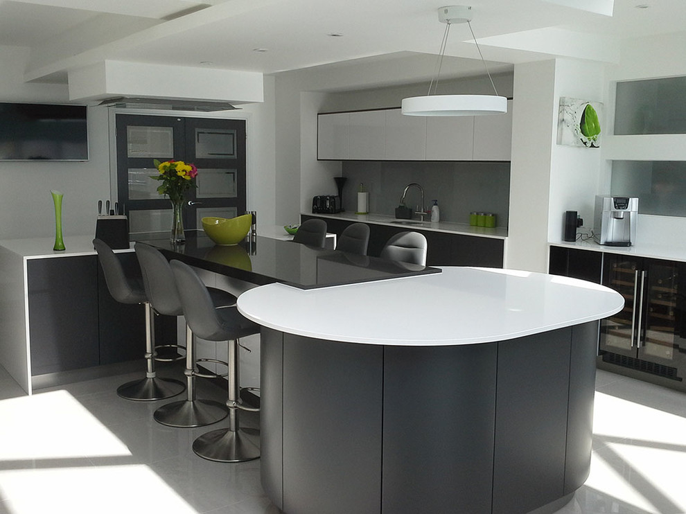 This is an example of a large contemporary u-shaped kitchen/diner in West Midlands with flat-panel cabinets, grey cabinets, quartz worktops, multiple islands, grey splashback, glass sheet splashback and stainless steel appliances.