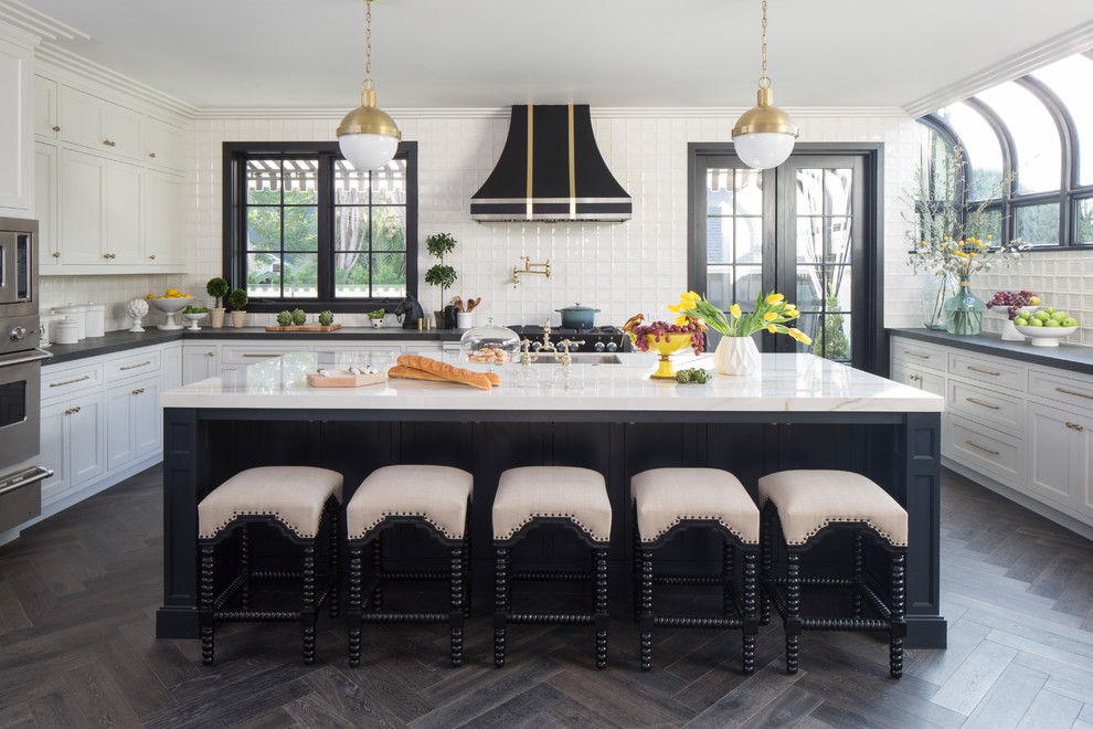 Inspiration for a transitional u-shaped dark wood floor and brown floor eat-in kitchen remodel in Los Angeles with an undermount sink, shaker cabinets, white cabinets, white backsplash, ceramic backsplash, stainless steel appliances and an island