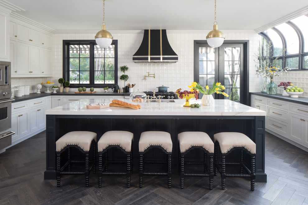 Diseño de cocina clásica renovada con fregadero bajoencimera, armarios estilo shaker, puertas de armario blancas, salpicadero blanco, salpicadero de azulejos de cerámica, electrodomésticos de acero inoxidable, suelo de madera oscura, una isla y suelo marrón