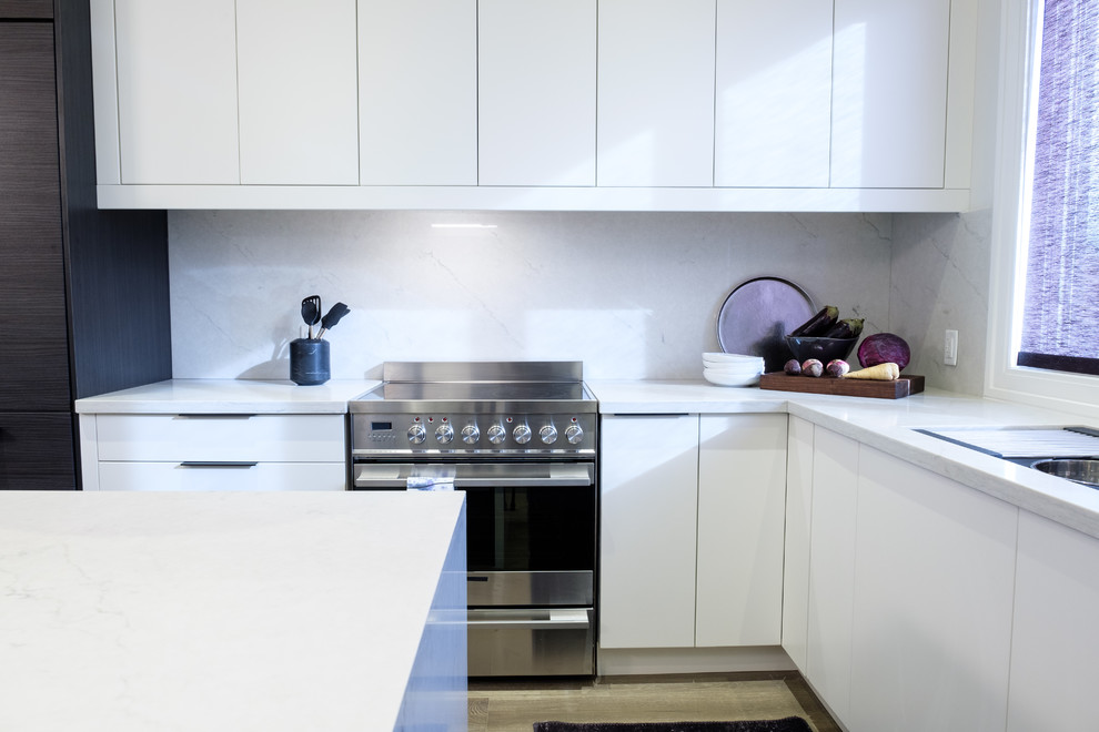 This is an example of a medium sized modern l-shaped kitchen/diner in Toronto with a double-bowl sink, flat-panel cabinets, white cabinets, quartz worktops, white splashback, stone slab splashback, stainless steel appliances, painted wood flooring, an island, beige floors and white worktops.