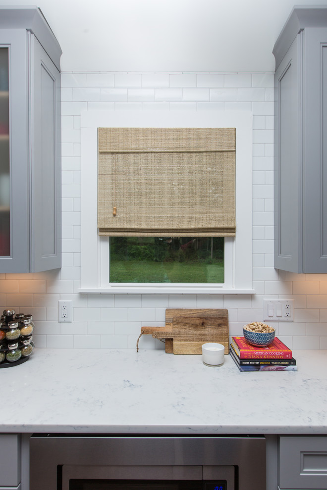 Exempel på ett mellanstort modernt kök, med en enkel diskho, luckor med profilerade fronter, grå skåp, bänkskiva i kvarts, vitt stänkskydd, stänkskydd i tunnelbanekakel, rostfria vitvaror, mörkt trägolv, en köksö och brunt golv