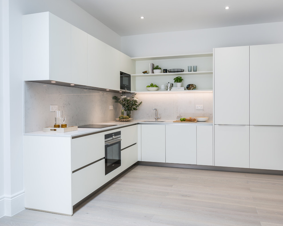 This is an example of a medium sized contemporary l-shaped kitchen/diner in Gloucestershire with an integrated sink, flat-panel cabinets, white cabinets, composite countertops, white splashback, stone slab splashback, black appliances, laminate floors, no island, brown floors and white worktops.