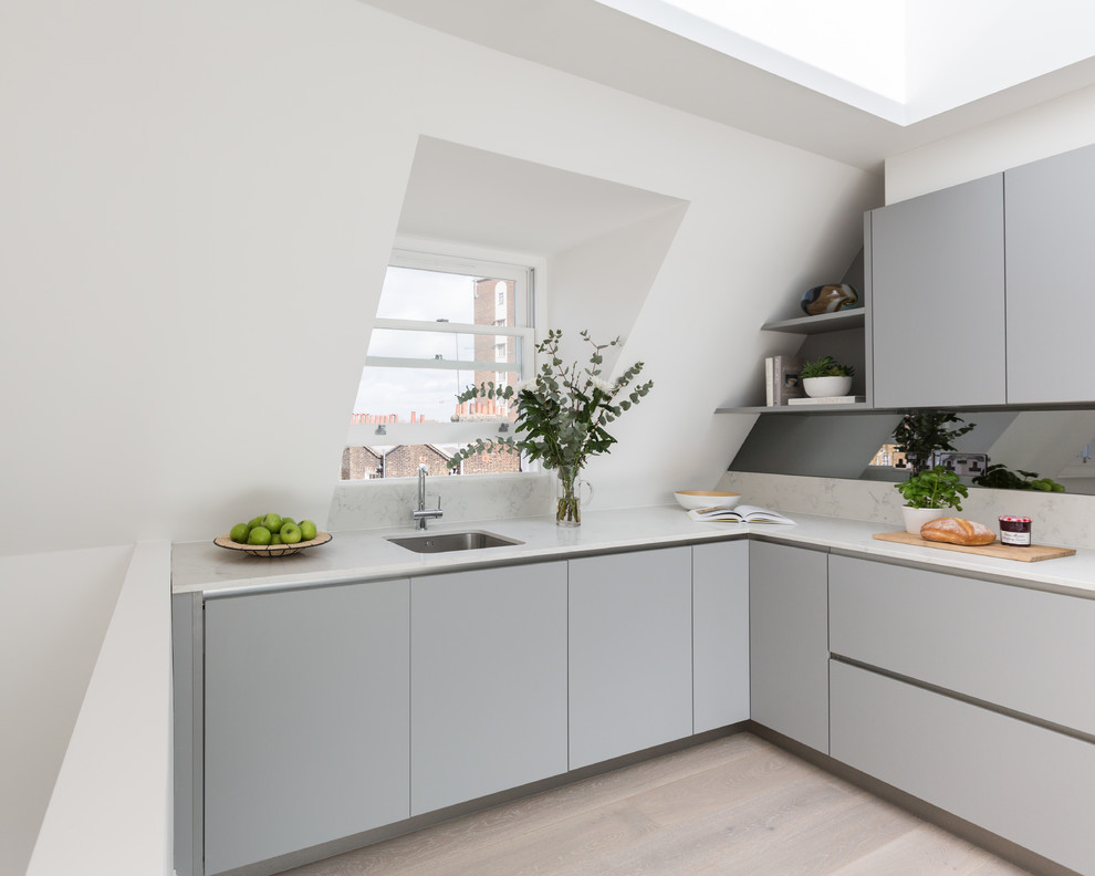 This is an example of a medium sized contemporary l-shaped kitchen in Gloucestershire with flat-panel cabinets, grey cabinets, composite countertops, mirror splashback, laminate floors, no island, white worktops, a submerged sink and beige floors.