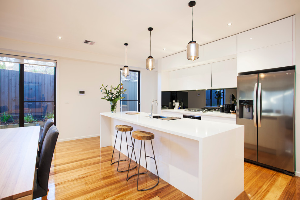 Zweizeilige Moderne Wohnküche mit Unterbauwaschbecken, flächenbündigen Schrankfronten, weißen Schränken, Mineralwerkstoff-Arbeitsplatte, Küchenrückwand in Schwarz, Küchengeräten aus Edelstahl, braunem Holzboden und Kücheninsel in Melbourne