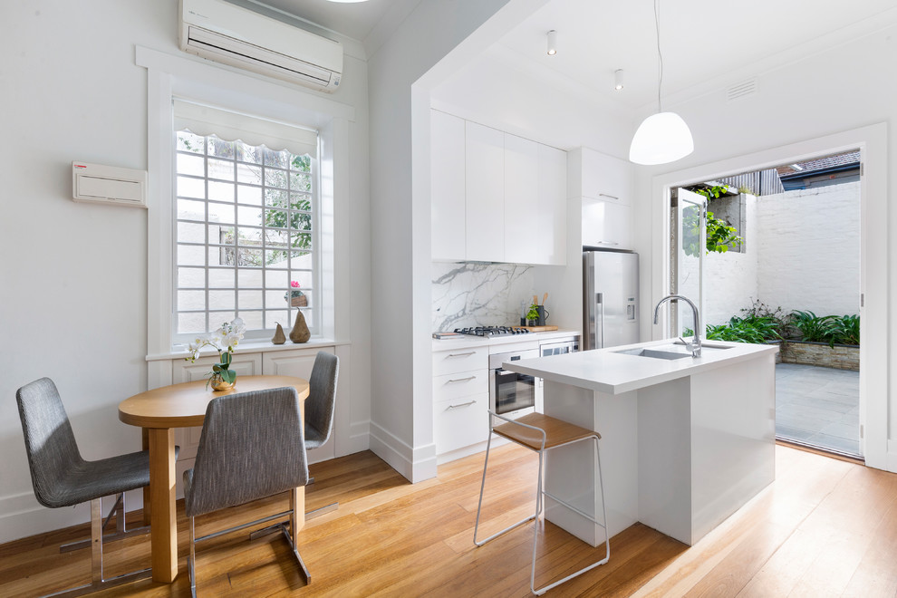 Medium sized traditional galley open plan kitchen in Melbourne with a built-in sink, white cabinets, engineered stone countertops, multi-coloured splashback, ceramic splashback, stainless steel appliances, medium hardwood flooring, an island, brown floors and white worktops.