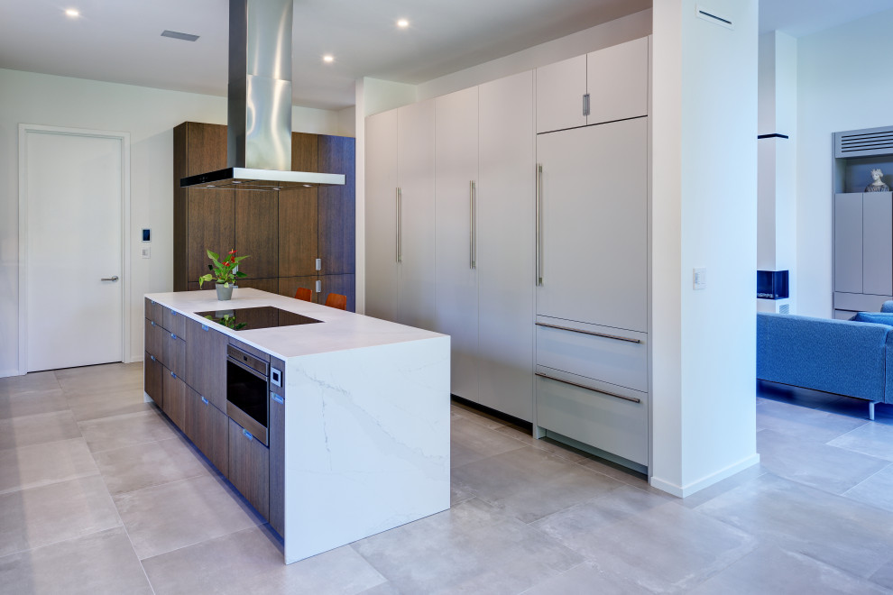 Modern inredning av ett stort vit vitt kök, med en undermonterad diskho, släta luckor, grå skåp, marmorbänkskiva, vitt stänkskydd, stänkskydd i marmor, integrerade vitvaror, betonggolv och en köksö