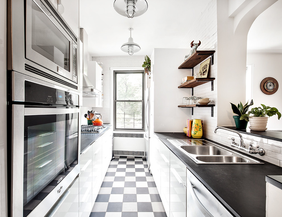 Transitional galley kitchen photo in New York with a double-bowl sink, flat-panel cabinets, white backsplash, subway tile backsplash and stainless steel appliances