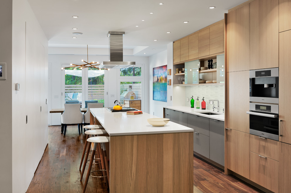 This is an example of a medium sized contemporary galley kitchen/diner in New York with a submerged sink, flat-panel cabinets, light wood cabinets, white splashback, dark hardwood flooring, an island, composite countertops and glass tiled splashback.