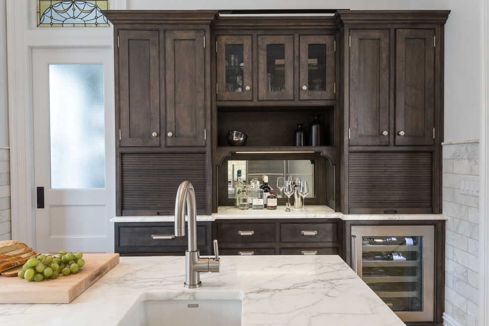 Inspiration for a mid-sized transitional l-shaped light wood floor enclosed kitchen remodel in New York with an undermount sink, shaker cabinets, dark wood cabinets, marble countertops, white backsplash, stone tile backsplash, stainless steel appliances and an island