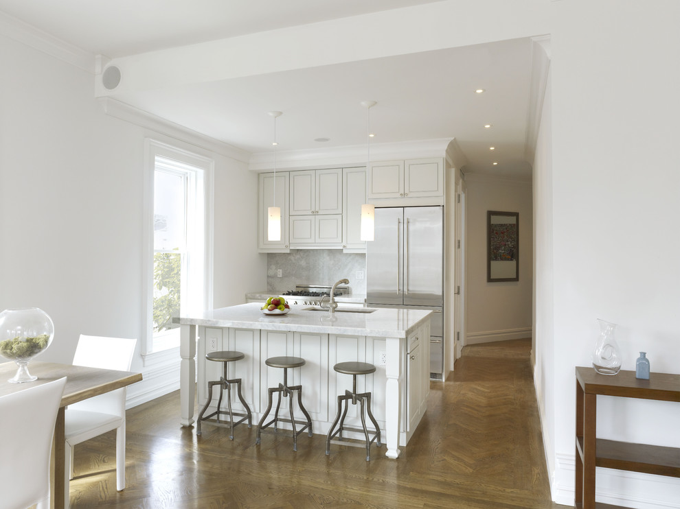 Foto på ett litet funkis kök, med rostfria vitvaror, en undermonterad diskho, luckor med infälld panel, vita skåp, bänkskiva i kvartsit, stänkskydd i sten, en köksö, mellanmörkt trägolv, grått stänkskydd och brunt golv
