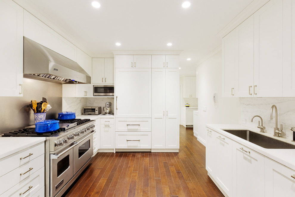 Inspiration for a transitional u-shaped enclosed kitchen remodel in New York with an undermount sink, shaker cabinets, white cabinets, metallic backsplash, metal backsplash, no island and paneled appliances