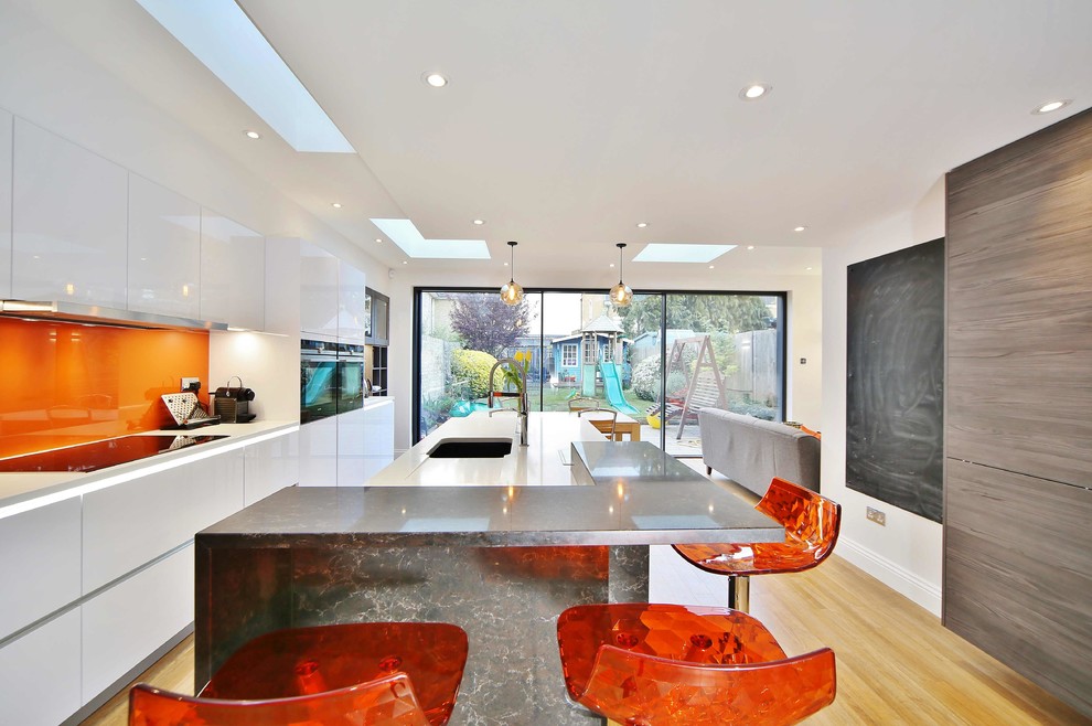 This is an example of a medium sized contemporary single-wall kitchen in London with a submerged sink, flat-panel cabinets, white cabinets, orange splashback, light hardwood flooring, an island and beige floors.