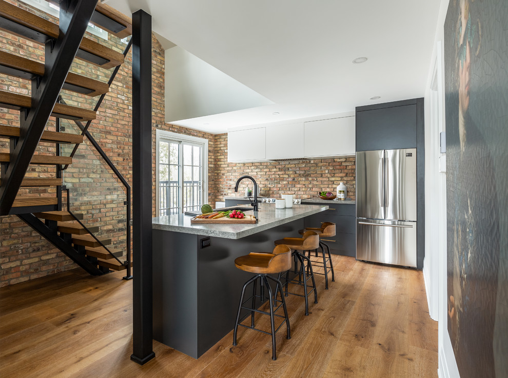 Example of a mid-sized urban l-shaped medium tone wood floor and brown floor kitchen design in Toronto with an undermount sink, flat-panel cabinets, quartz countertops, brick backsplash, stainless steel appliances, an island, gray countertops and gray cabinets
