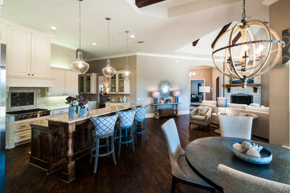 Mid-sized trendy l-shaped dark wood floor and brown floor open concept kitchen photo in Dallas with raised-panel cabinets, distressed cabinets, granite countertops, beige backsplash, stone tile backsplash, stainless steel appliances and an island