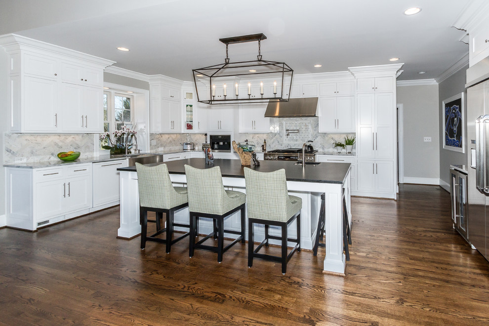 Kitchen - large traditional l-shaped dark wood floor kitchen idea in Charlotte with a farmhouse sink, shaker cabinets, gray backsplash, stainless steel appliances and an island