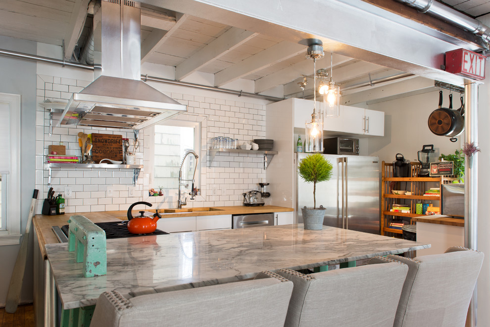 Example of an eclectic kitchen design in Providence with a double-bowl sink, flat-panel cabinets, white cabinets, wood countertops, white backsplash, subway tile backsplash, stainless steel appliances and an island