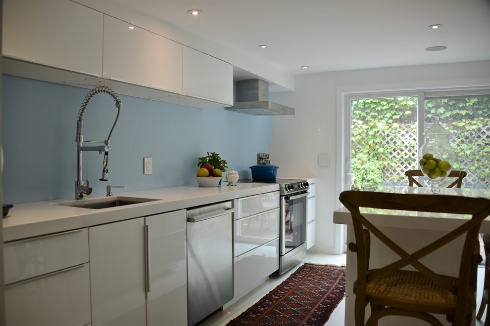 Foto på ett litet vintage kök, med en undermonterad diskho, släta luckor, vita skåp, bänkskiva i kvarts, blått stänkskydd, rostfria vitvaror och målat trägolv