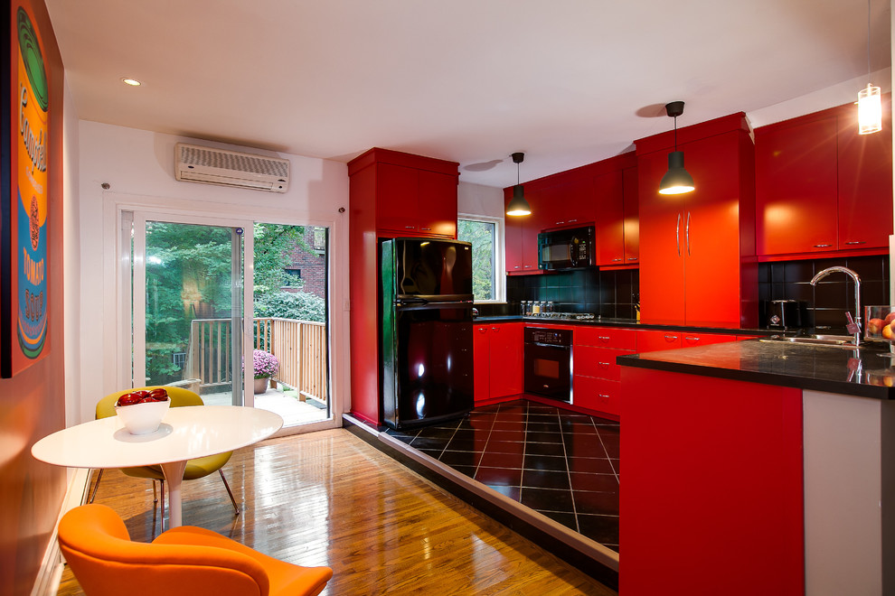 На фото: кухня в современном стиле с обеденным столом, плоскими фасадами, красными фасадами, черным фартуком и черной техникой