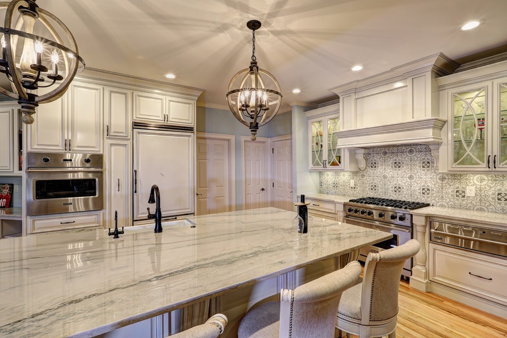 This is an example of a large classic l-shaped open plan kitchen in Atlanta with a belfast sink, raised-panel cabinets, white cabinets, quartz worktops, grey splashback, ceramic splashback, stainless steel appliances, light hardwood flooring, an island, beige floors and white worktops.