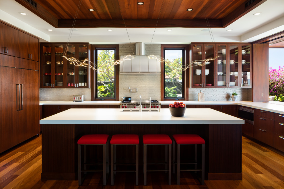 Design ideas for a contemporary u-shaped kitchen in Hawaii with a submerged sink, flat-panel cabinets, dark wood cabinets, white splashback, stainless steel appliances, medium hardwood flooring, an island, brown floors and white worktops.