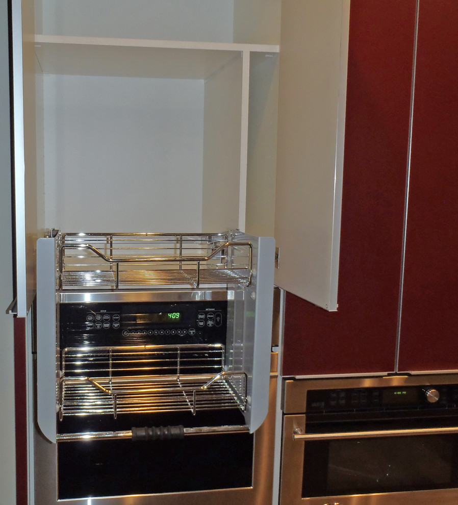 Modern inredning av ett kök, med en undermonterad diskho, släta luckor, röda skåp, marmorbänkskiva, stänkskydd med metallisk yta, stänkskydd i porslinskakel och rostfria vitvaror