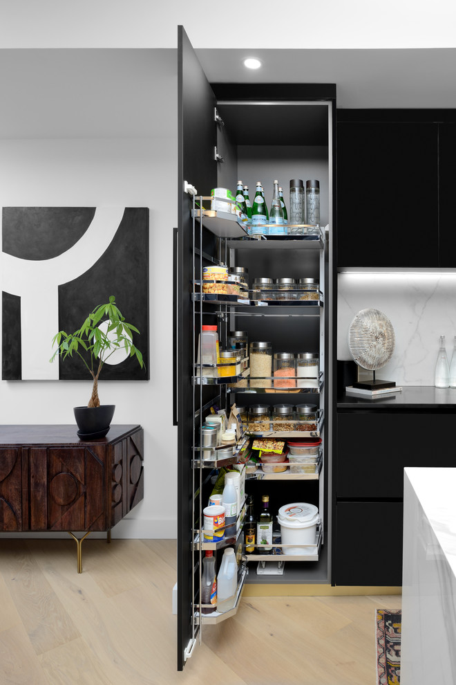Diseño de cocina actual con armarios con paneles lisos, puertas de armario negras, salpicadero blanco, suelo de madera clara, suelo beige y encimeras negras