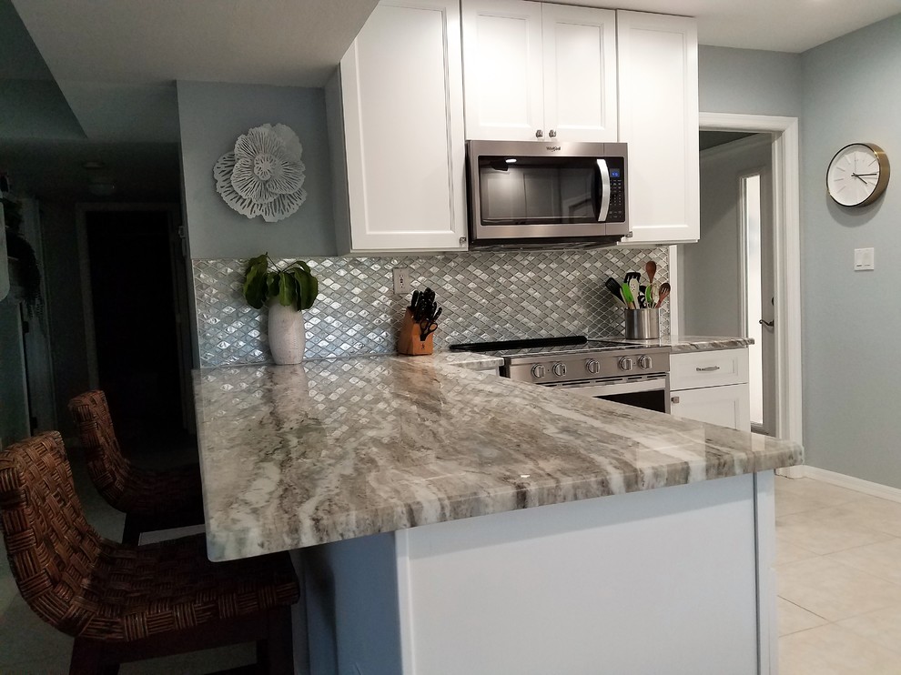 Inredning av ett maritimt mellanstort grå grått kök, med en undermonterad diskho, luckor med infälld panel, vita skåp, marmorbänkskiva, grått stänkskydd, stänkskydd i mosaik, rostfria vitvaror, klinkergolv i porslin, en köksö och vitt golv