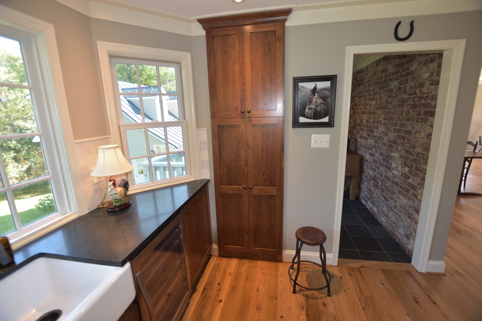 Modelo de cocina de estilo de casa de campo grande abierta con armarios con paneles lisos, puertas de armario de madera oscura, encimera de esteatita y una isla