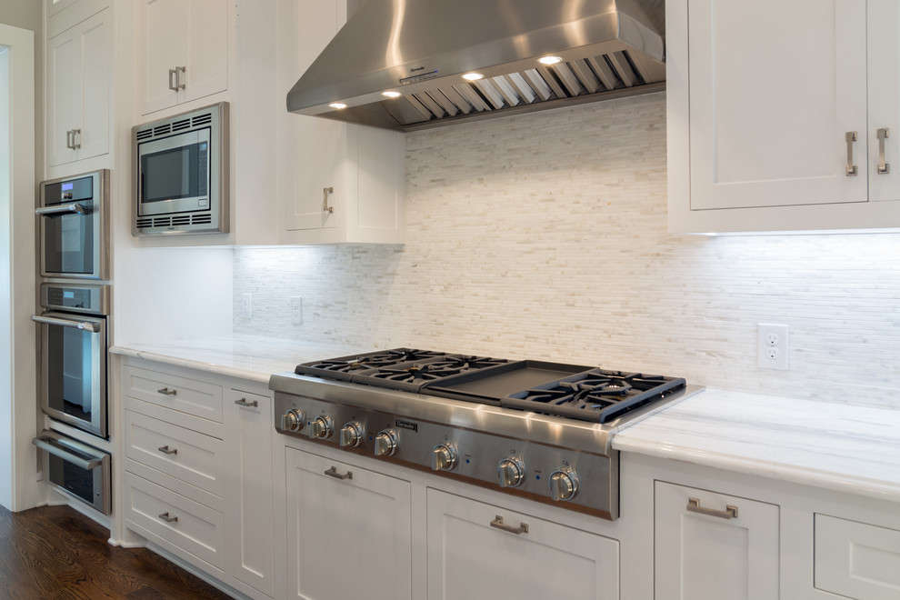 Large transitional l-shaped dark wood floor open concept kitchen photo in Dallas with an undermount sink, recessed-panel cabinets, white cabinets, marble countertops, white backsplash, stone tile backsplash, stainless steel appliances and two islands