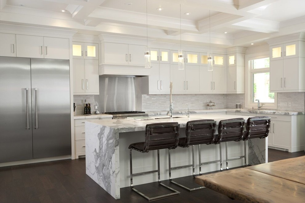 Bild på ett stort funkis kök, med en undermonterad diskho, släta luckor, vita skåp, marmorbänkskiva, vitt stänkskydd, stänkskydd i stenkakel, rostfria vitvaror, mellanmörkt trägolv och en köksö