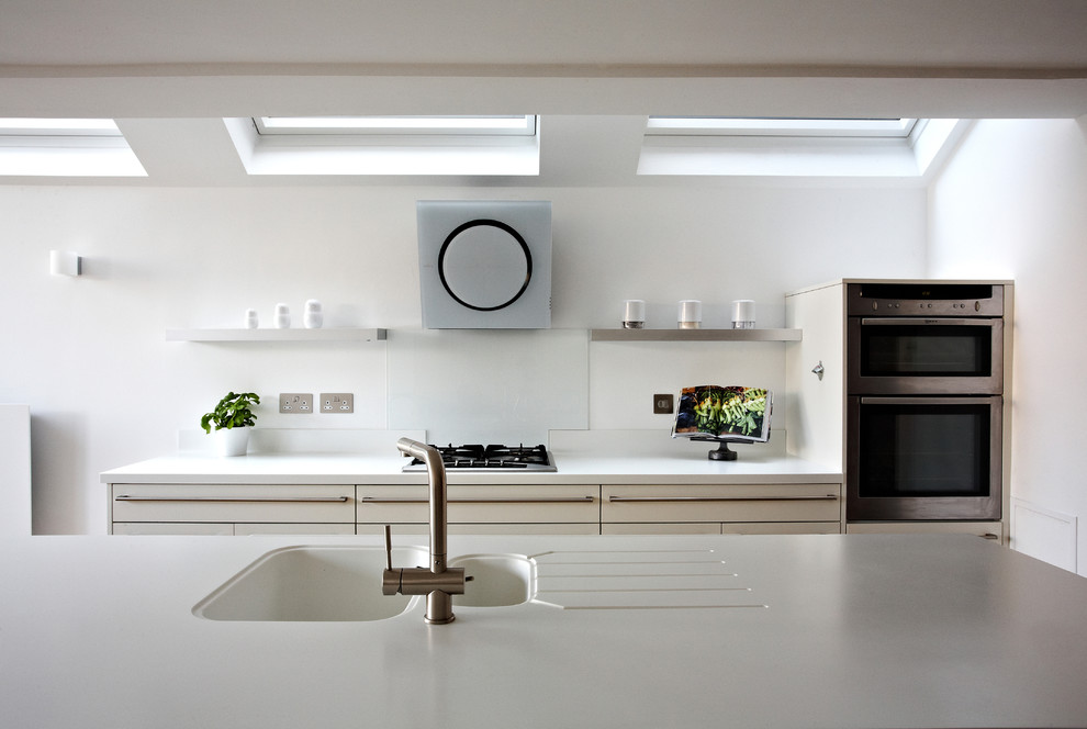 Moderne Wohnküche mit integriertem Waschbecken, flächenbündigen Schrankfronten, weißen Schränken, Küchenrückwand in Weiß, Küchengeräten aus Edelstahl, braunem Holzboden und Kücheninsel in Sonstige